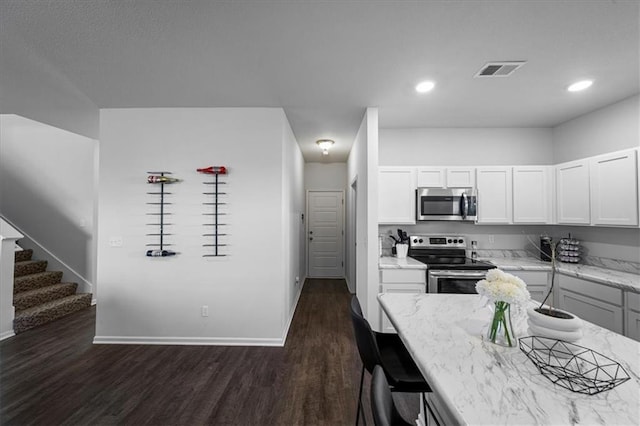 kitchen with appliances with stainless steel finishes, white cabinetry, light stone counters, and dark wood-type flooring