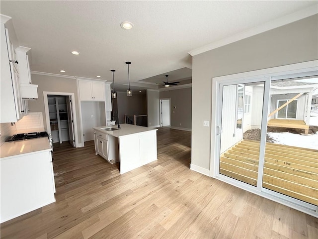 kitchen featuring sink, crown molding, white cabinetry, hanging light fixtures, and a center island with sink