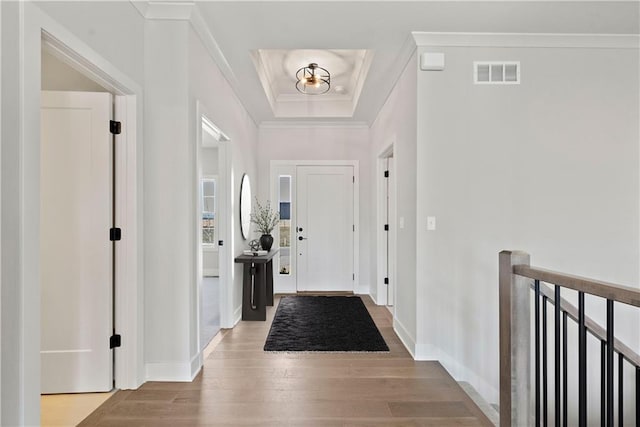 entrance foyer with ornamental molding, light hardwood / wood-style floors, and a tray ceiling