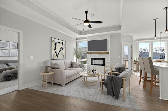 living room with dark wood-type flooring, ornamental molding, a healthy amount of sunlight, and a tray ceiling