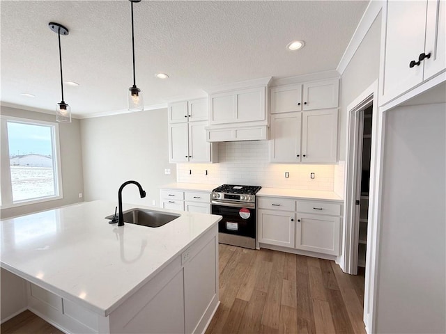 kitchen with stainless steel gas stove, sink, hanging light fixtures, and white cabinets