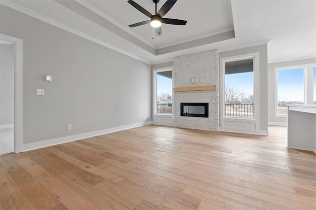 unfurnished living room featuring ceiling fan, ornamental molding, a tray ceiling, and light wood-type flooring