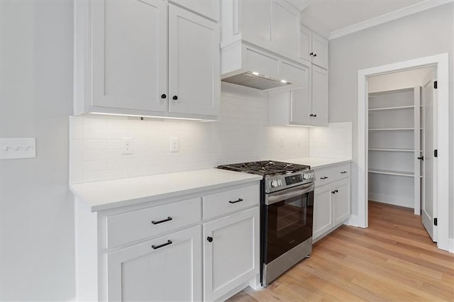 kitchen with light wood finished floors, white cabinetry, backsplash, light countertops, and stainless steel gas range oven