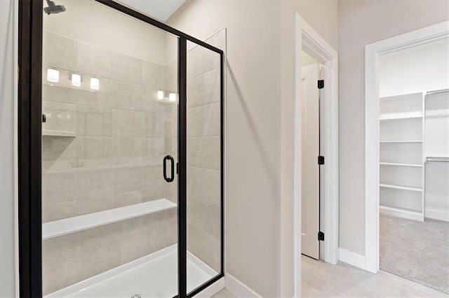 bathroom featuring baseboards, a walk in closet, and a stall shower
