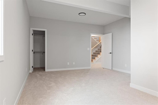unfurnished bedroom featuring baseboards, a spacious closet, and light colored carpet