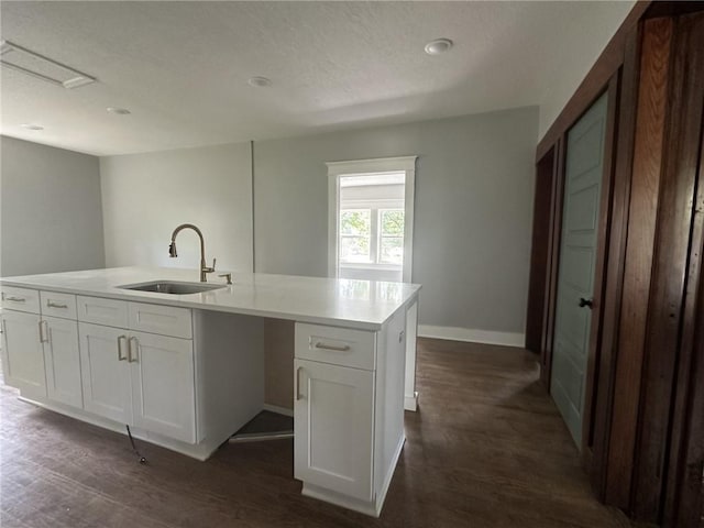 kitchen with sink, an island with sink, a textured ceiling, white cabinets, and dark hardwood / wood-style floors