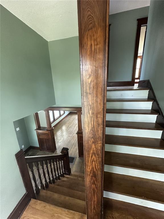 staircase featuring a textured ceiling, baseboards, and wood finished floors