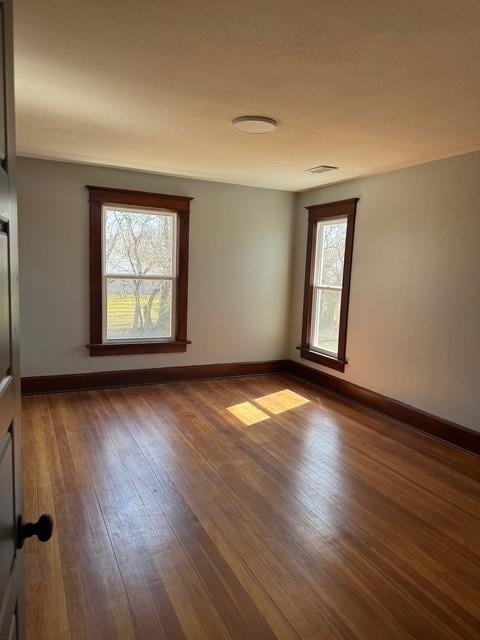 empty room featuring visible vents, baseboards, and wood-type flooring