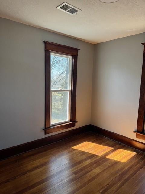 unfurnished room featuring baseboards, visible vents, and dark wood-style flooring