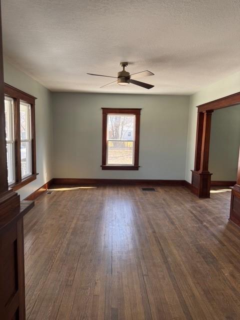 empty room with visible vents, baseboards, a textured ceiling, and dark wood finished floors