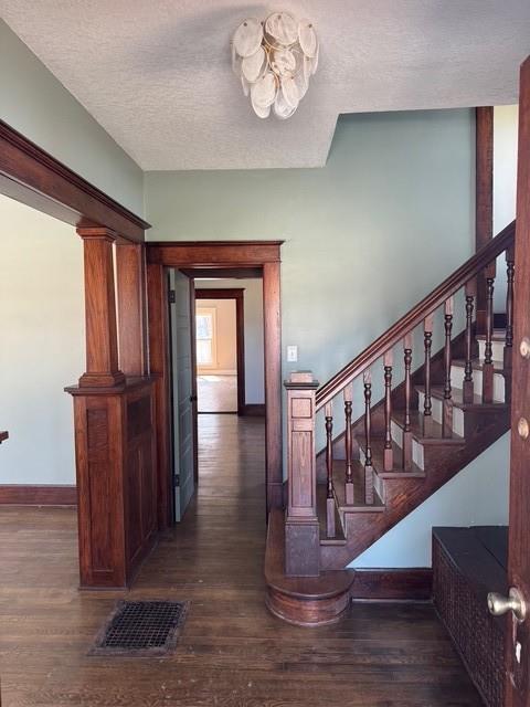 staircase featuring visible vents, a textured ceiling, baseboards, and wood finished floors