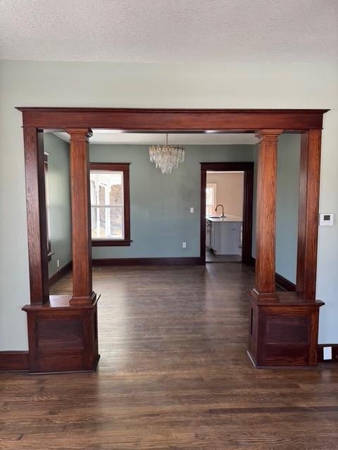 interior space featuring baseboards, a textured ceiling, ornate columns, and dark wood-style flooring