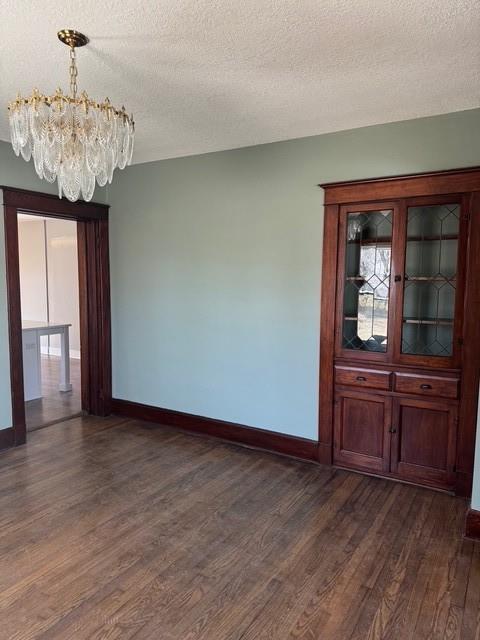 unfurnished room with baseboards, a textured ceiling, dark wood-type flooring, and an inviting chandelier