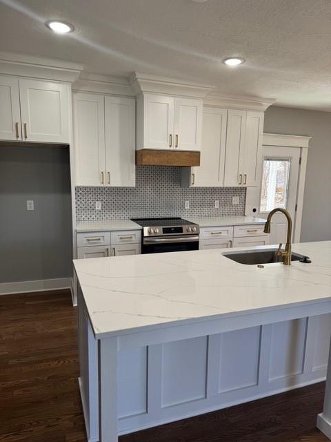 kitchen with stainless steel electric range oven, light stone countertops, a sink, white cabinetry, and backsplash