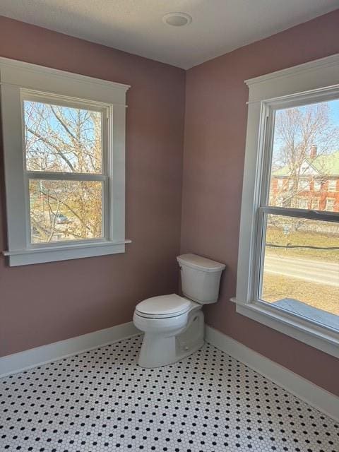 bathroom with a wealth of natural light, baseboards, and toilet