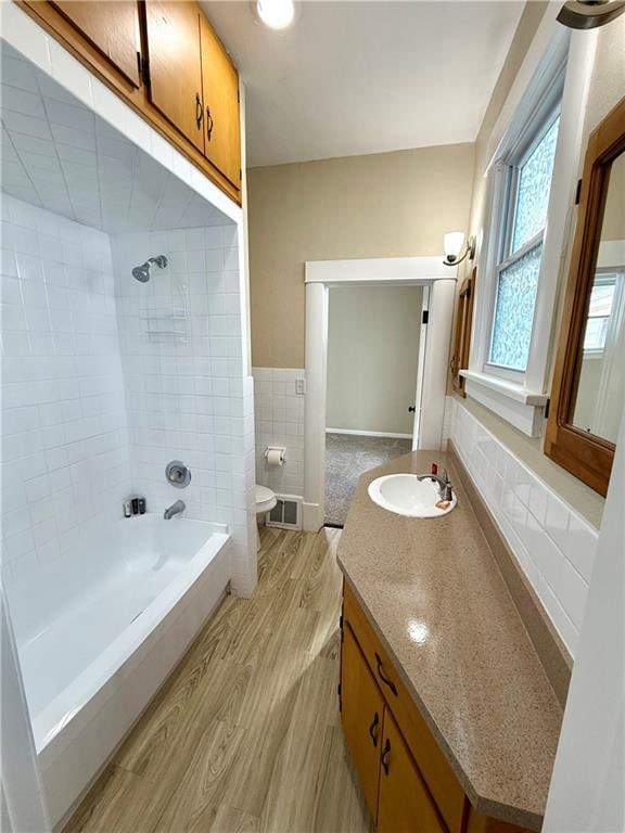 full bathroom with vanity, tiled shower / bath, toilet, tile walls, and wood-type flooring