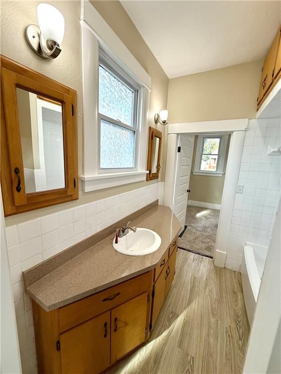 bathroom featuring hardwood / wood-style flooring, vanity, a healthy amount of sunlight, and tile walls