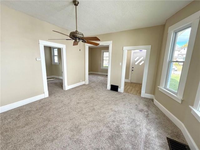 unfurnished bedroom featuring light carpet, a textured ceiling, multiple windows, and ceiling fan