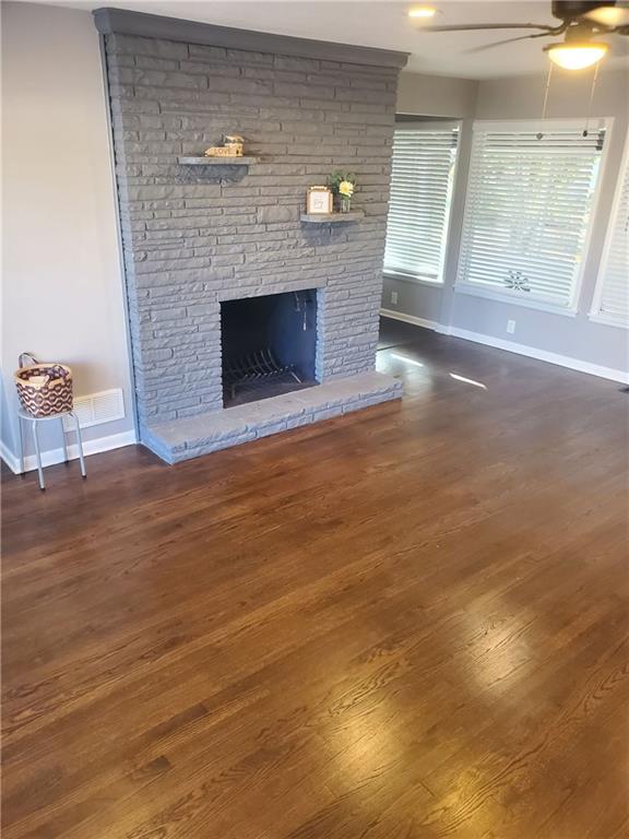 unfurnished living room featuring a stone fireplace, ceiling fan, and dark hardwood / wood-style floors