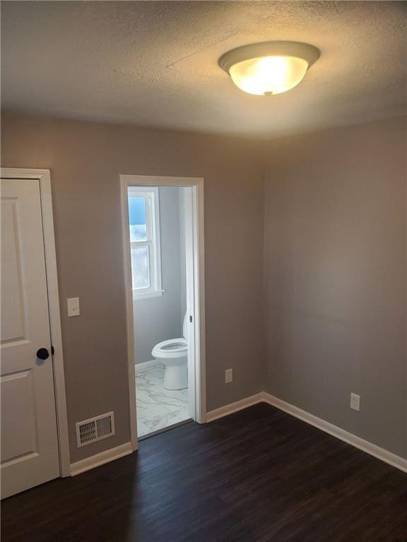 unfurnished bedroom featuring dark wood-type flooring, a textured ceiling, and ensuite bath