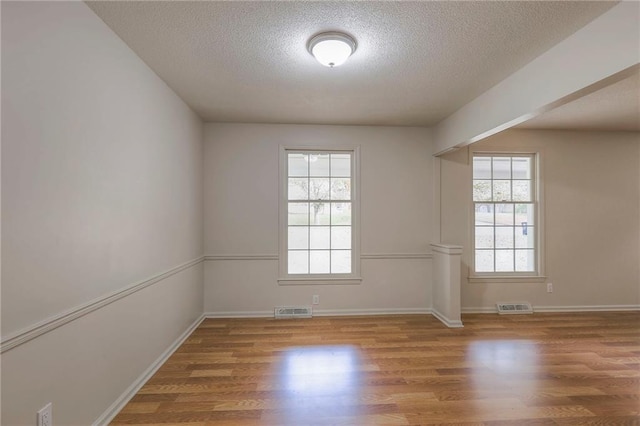 spare room with a textured ceiling, wood-type flooring, and plenty of natural light