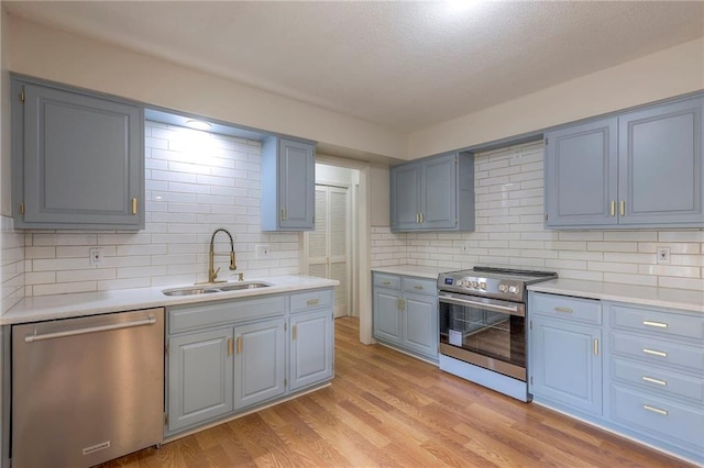 kitchen featuring sink, backsplash, a textured ceiling, stainless steel appliances, and light hardwood / wood-style flooring