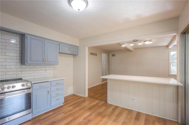 kitchen featuring a textured ceiling, kitchen peninsula, light hardwood / wood-style floors, stainless steel stove, and decorative backsplash