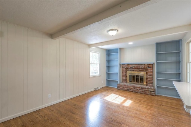 unfurnished living room featuring hardwood / wood-style floors, a brick fireplace, wood walls, beamed ceiling, and built in features