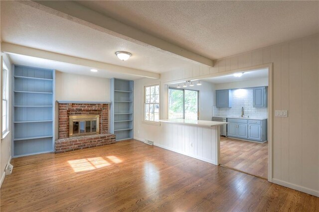 unfurnished living room featuring beam ceiling, a textured ceiling, wood-type flooring, a fireplace, and sink