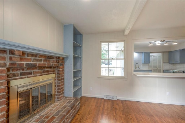 unfurnished living room with hardwood / wood-style flooring, beamed ceiling, sink, and a brick fireplace