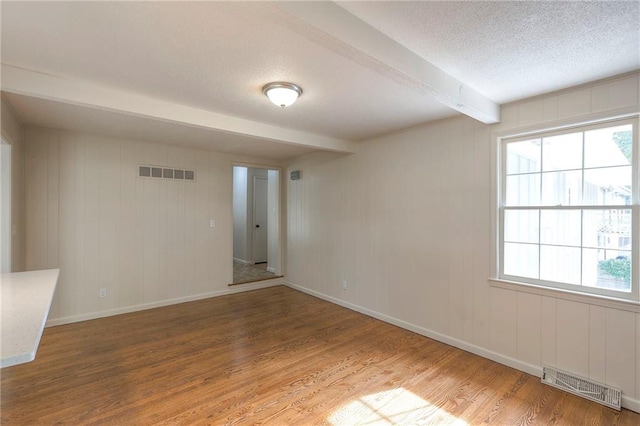 empty room with beam ceiling, a textured ceiling, and hardwood / wood-style floors