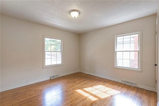 empty room with a textured ceiling and light hardwood / wood-style flooring