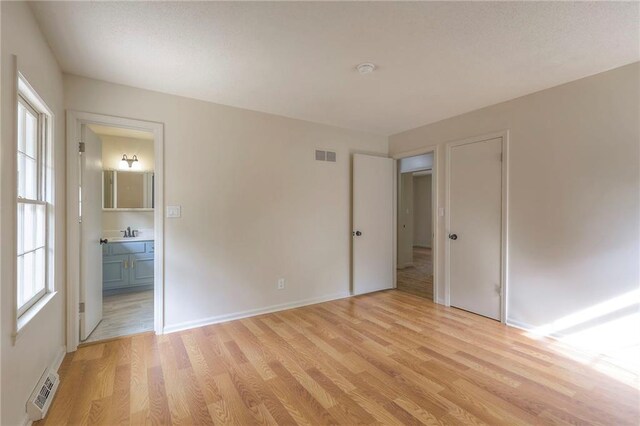 unfurnished bedroom with light hardwood / wood-style flooring, a closet, sink, and connected bathroom