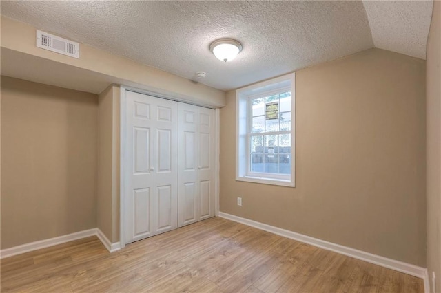 unfurnished bedroom featuring lofted ceiling, a textured ceiling, light wood-type flooring, and a closet