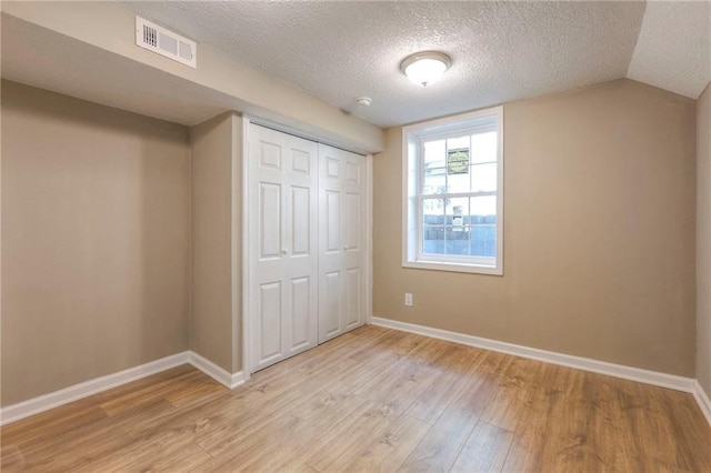 unfurnished bedroom with a closet, lofted ceiling, a textured ceiling, and light hardwood / wood-style flooring