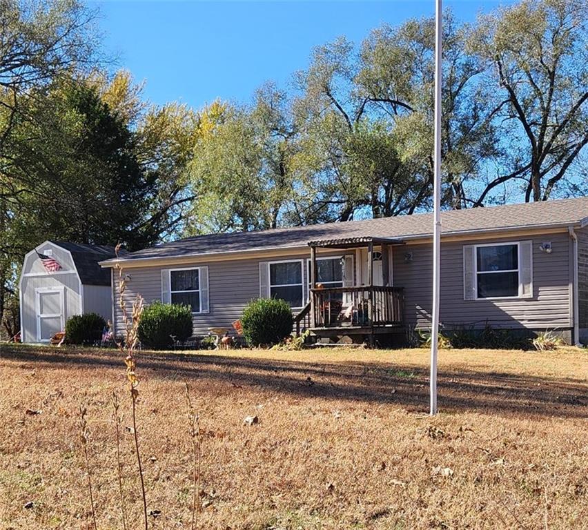 single story home with a deck, a front lawn, and a storage shed