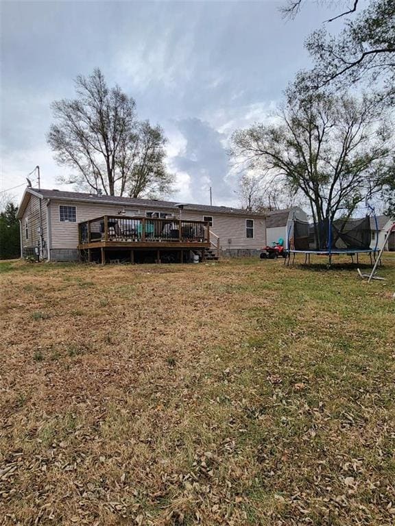 rear view of property with a lawn, a trampoline, and a deck