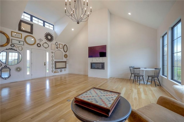 living room featuring high vaulted ceiling, a chandelier, wood finished floors, and a glass covered fireplace