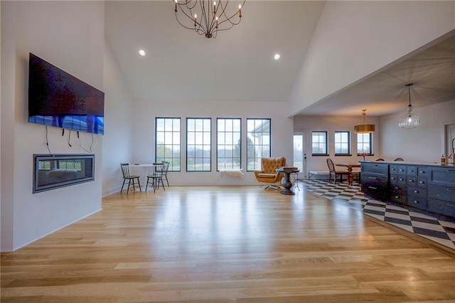 living area featuring a chandelier, a glass covered fireplace, light wood-style floors, high vaulted ceiling, and recessed lighting