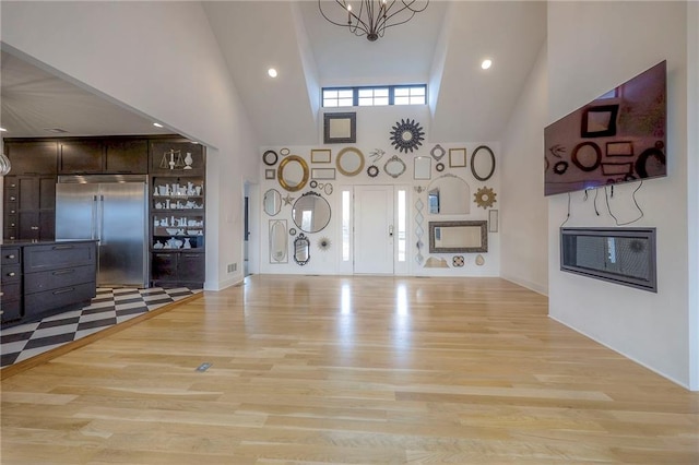 unfurnished living room with recessed lighting, a high ceiling, a notable chandelier, and light wood finished floors