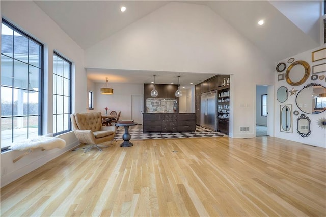 living area with light wood finished floors, baseboards, visible vents, and high vaulted ceiling