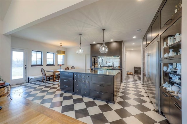 kitchen featuring dark countertops, decorative light fixtures, dark floors, and a kitchen island with sink