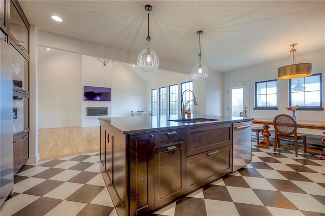 kitchen featuring dark brown cabinetry, a center island with sink, dishwasher, pendant lighting, and a sink