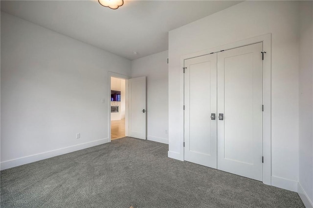 unfurnished bedroom with dark colored carpet, a closet, and baseboards