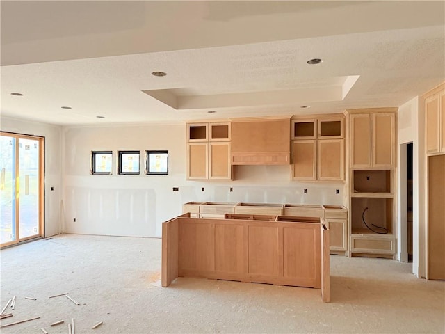 kitchen featuring a raised ceiling, light brown cabinetry, a kitchen island, and light colored carpet