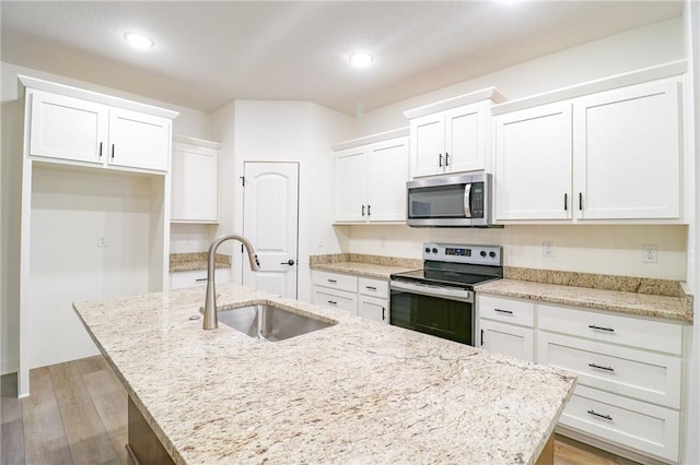 kitchen with a center island with sink, sink, white cabinets, light wood-type flooring, and appliances with stainless steel finishes