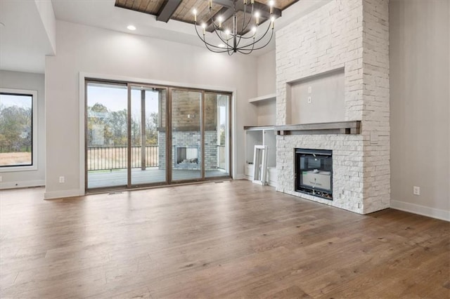 unfurnished living room with a towering ceiling, wood-type flooring, a stone fireplace, beam ceiling, and an inviting chandelier