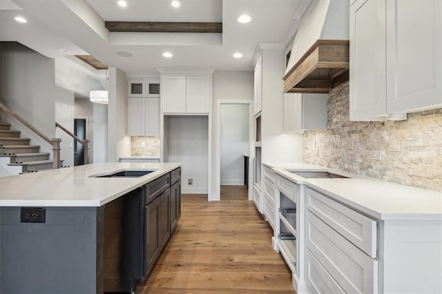 kitchen featuring white cabinets, tasteful backsplash, light wood-type flooring, custom range hood, and a center island