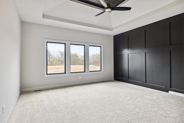 unfurnished bedroom with light carpet, a tray ceiling, and ceiling fan