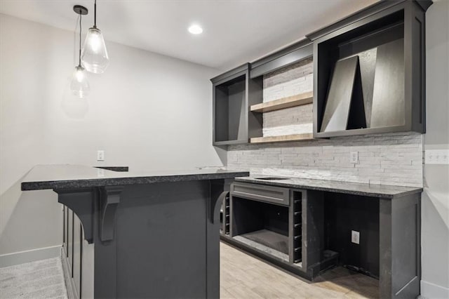 kitchen with kitchen peninsula, backsplash, a breakfast bar, dark stone countertops, and pendant lighting